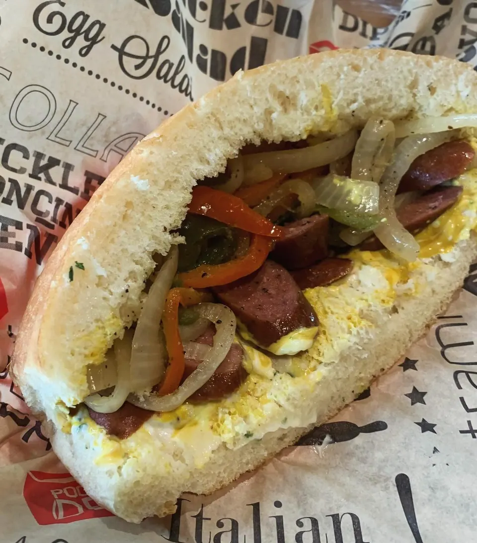 Sandwich with eggs, sausage, grilled onions, and bell peppers on a hoagie bun.